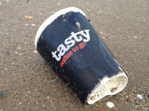 Single use coffee cup abandoned on beach